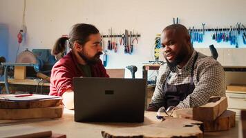 möbelsnickare håller på med brainstorming medan använder sig av cad programvara på bärbar dator, diskuterar trä mönster. snickare i hopsättning affär diskuterar, använder sig av program på anteckningsbok till planen möbel montering, kamera b foto