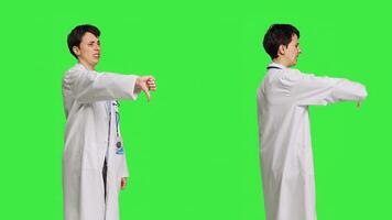 missnöjd läkare som visar tummen ner symbol mot grönskärm bakgrund, uttrycker negativitet och avslag. läkare känsla missnöjd och håller inte med med ett aning, motvilja tecken. kamera b. foto