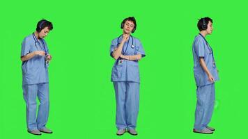 glad hälsa specialist lyssnande till Häftigt musik på audio headset, dans mot grönskärm bakgrund och har roligt. sjuksköterska njuter låtar ett håller på med rolig dansa rör sig, fritid. kamera a. foto