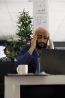 utmattad arab entreprenör med migrän skrivning företag planen på bärbar dator i kontor. överarbetad anställd har huvudvärk medan analyserar Start upp företag marknadsföring strategi foto