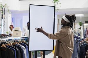 kund använder sig av tömma vit smart skärm till bläddra kläder i Lagra. afrikansk amerikan eleganta man rörande interaktiv tom visa medan handla för kläder i köpcenter boutique foto