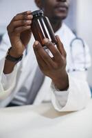närbild skott visar en svart man bär en labb täcka och klämmer fast en recept piller. selektiv fokus av ett afrikansk amerikan läkare innehav en flaska av medicin för patient behandling. foto