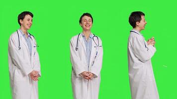 porträtt av allmän praktiker skrattande på något mot grönskärm bakgrund, känsla glad och självsäker med henne sjukvård expertis. kvinna läkare i vit täcka leende i studio. kamera b. foto