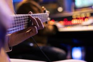 begåvad sångare spelar ny överenskommelser på elektro akustisk gitarr i musik studio, inspelning ny låtar med audio ingenjör i kontrollera rum. manlig musiker producerar spår på instrument. stänga upp. foto