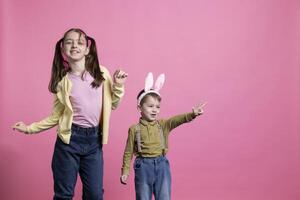 ljuv liten barn har roligt med dansa rör sig i studio, lurar runt om och känsla Lycklig handla om påsk Semester fest. förtjusande småbarn syskon dans i främre av kamera, kanin öron. foto