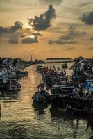 jepara, central java, april 7, 2024 - jepara fiske båtar parkerad i en fullt med folk hamn mot de bakgrund av de kväll himmel med tömma Plats för reklam foto