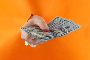 dollar pengar hand genom en hål i ett orange kartong foto