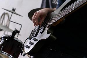 en man spelar en bas gitarr i en tillfällig miljö. han är fokuserade på hans instrument, fingrar glidande över de strängar. hans avslappnad hållning och tillfällig klädsel föreslå en avslappnad musik session. foto