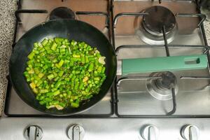 färsk grön sparris tärnad och fräsande i en stekpanna på de spis. foto