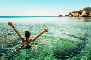 kvinna njut av semester simma i nordlig Cypern. ayia napa bukt Strand med kristall klar blå medelhavs vattnen och marinmålning klippig sten Strand. hav grottor populär resa destination foto