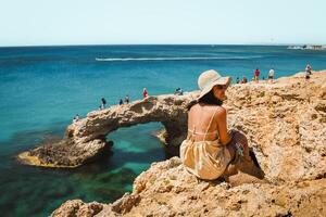 kvinna turist sitta på synpunkt sightseeing cypern grekisk ö besök sten båge eller bro av kärlek. känd Semester destination i medelhavs havskust foto