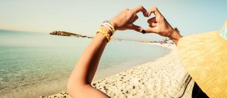 Lycklig flicka turist på solig nissi strand i cypern visa finger formad hjärta form tecken. händer av flicka form av hjärta. sommar dröm. lycka av frihet på högtider semester foto
