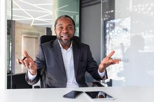 ring upp uppkopplad möte, afrikansk amerikan affärsman chef leende och ser på kamera, man i företag kostym mogna har roligt talande med kollegor, på virtuell möte inuti kontor avlägset. foto