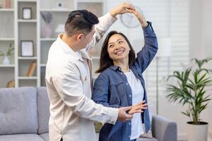 Lycklig asiatisk par, ung familj man och kvinna fira rör på sig till en ny hus, uppköp ett lägenhet. de dansa, kram, skratt. foto