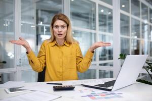 frustrerad och ledsen arbetsplats kvinna inuti kontor arbetsplats ser på kamera, affärskvinna olycklig med arbete och prestation resultat, nervös arbetssätt med bärbar dator. foto