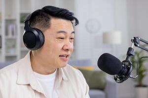 asiatisk manlig podcaster tala in i en mikrofon medan inspelning innehåll för hans podcast i en mysigt Hem studio miljö. foto