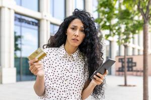 bekymrad ung latin amerikan affärskvinna med kreditera kort och telefon på stad gata, finansiell problem begrepp. foto