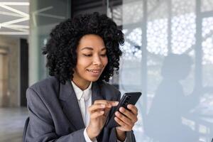 framgångsrik affärskvinna användningar smartphone inuti kontor närbild, leende anställd användningar app på telefon, typer meddelanden och bläddrar internet sidor uppkopplad. foto