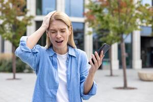 mogna kvinna utanför kontor byggnad i blå skjorta ledsen mottagen uppkopplad meddelande, kvinna arbetstagare läsning dålig Nyheter använder sig av app på telefon, visning social media mobbning och trakasserier. foto