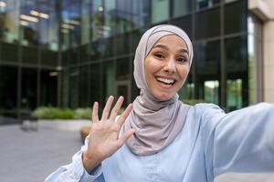 glad kvinna i en hijab fångande en selfie ögonblick utomhus med en hög fem gest och glad uttryck. foto