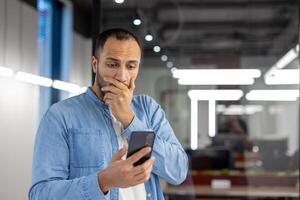 indisk affärsman fokuserade på läsning innehåll på hans smartphone inuti de modern kontor miljö. foto