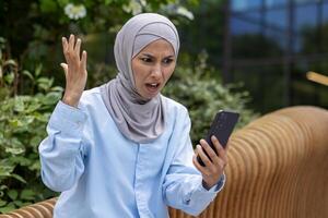 upprörd ledsen kvinna mottagen uppkopplad underrättelse meddelande med dålig Nyheter, muslim kvinna i hijab innehav telefon, använder sig av app. foto