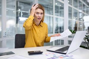 porträtt av frustrerad och upprörd kvinna finansiär inuti kontor på arbetsplats, företag kvinna ser missnöjd på kamera innehav finansiell rapporter och kontrakt med grafer och diagram i händer. foto