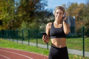 atletisk kvinna i träna redskap använder sig av telefon med hörlurar på solig dag på sporter Spår. kondition och teknologi begrepp. foto