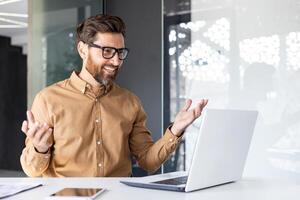 uppkopplad ringa upp, avlägsen konversation, man leende på presentation talande till kollegor och partners, affärsman arbetssätt inuti kontor med bärbar dator, bär skjorta och glasögon. foto