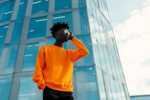 porträtt av ett attraktiv svart afro amerikan manlig modell bär orange tom attrapp crewneck tröja och Framställ i främre av en modern kontor byggnad exteriör foto