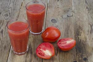 glasögon med färsk juice av mogna röda tomater på träbord foto