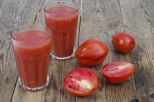 glasögon med färsk juice av mogna röda tomater på träbord foto