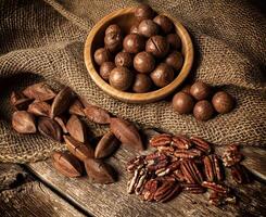 macadamia, pekannöt och pili nötter på trä- tabell foto