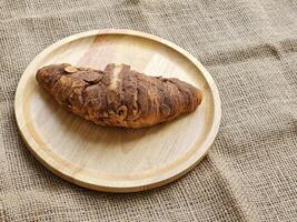 choklad croissanter dekorerad med kakao pulver och mandlar på en trä- tallrik. sida se foto