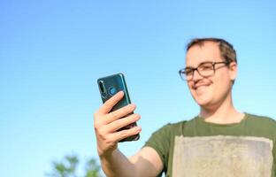 man med glasögon och grön t-shirt på ring upp från hans cell telefon på parkera foto