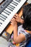 asiatisk söt flicka spelar de synthesizer eller piano. söt liten unge inlärning på vilket sätt till spela piano. barnets händer på de tangentbord inomhus. foto
