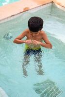 Lycklig indisk pojke simning i en slå samman, unge bär simning kostym längs med luft rör under varm sommar semester, barn pojke i stor simning slå samman. foto