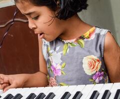 asiatisk söt flicka spelar de synthesizer eller piano. söt liten unge inlärning på vilket sätt till spela piano. barnets händer på de tangentbord inomhus. foto