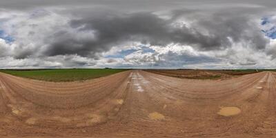 hdri 360 panorama på våt grus väg med vattenpölar bland fält i vår otäck dag med storm moln i likriktad full sömlös sfärisk utsprång, för vr ar virtuell verklighet innehåll foto