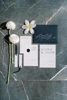 bröllop inbjudningar, namn kort och vit blommor lögn på en svart marmor tabell foto
