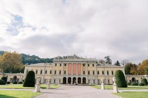 parkera med statyer i främre av de gammal villa olmo med tömma banderoller på de Fasad. sjö como, Italien foto