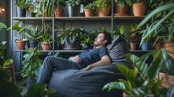 en man slappnar av på en bönpåse stol omgiven förbi hyllor av inomhus- växter den där han kärleksfullt bryr sig för foto