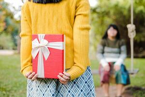 flicka innehav en röd gåva låda stående i de trädgård foto