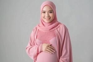 strålnings förväntans mor i mjuk rosa hijab fattande moderskap foto