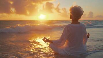 som de Sol stiger över de horisont ett äldre kvinna omfamnar de lugnande energi av de hav som hon flöden genom en föryngrande yoga rutin- på de fredlig strand foto