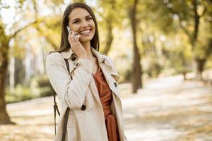 glad ung kvinna som använder mobiltelefon i höst park foto