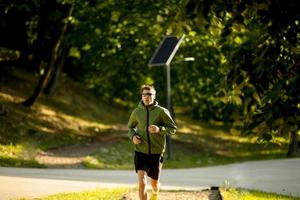 atletisk ung man kör medan du tränar i solig grön park foto