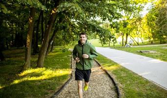 atletisk ung man kör medan du tränar i solig grön park foto