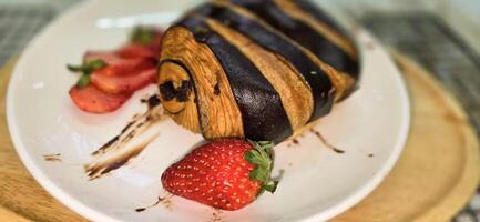 färsk hemlagad randig choklad croissant med choklad fyllning på en runda vit tallrik, eras med färsk jordgubb foto