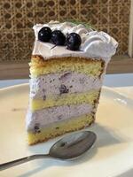 skiva av blåbär kaka dekorerad med färsk bär på vit tallrik, utsökt skiktad kaka, topp se foto